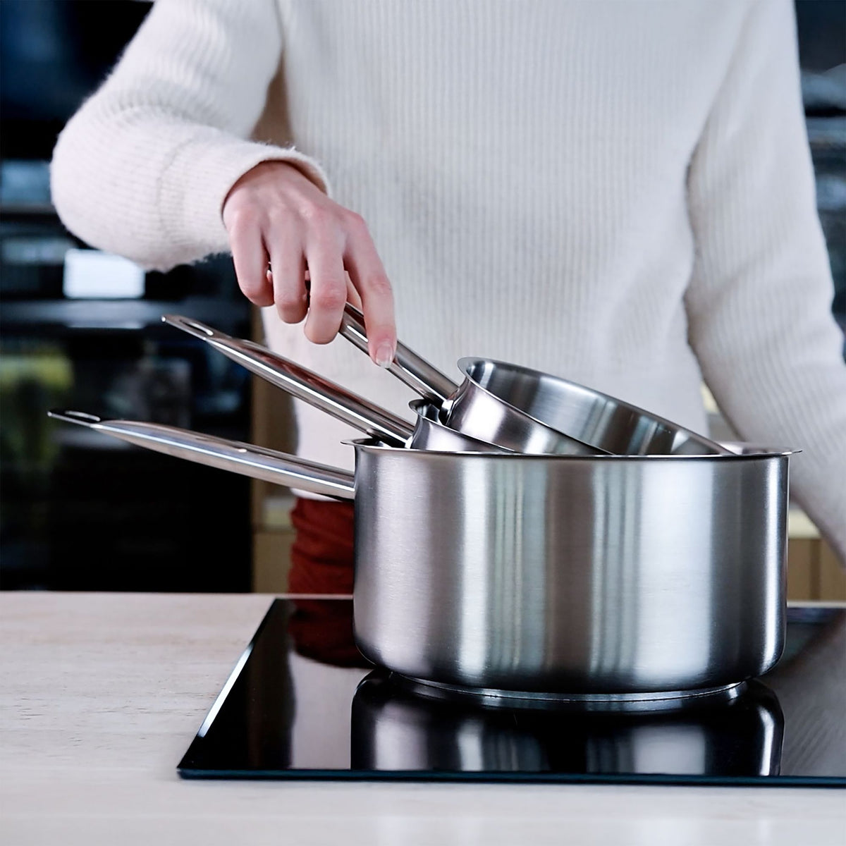 Personne en pull blanc soulevant le couvercle d'une casserole inox professionnelle sur plaque de cuisson
