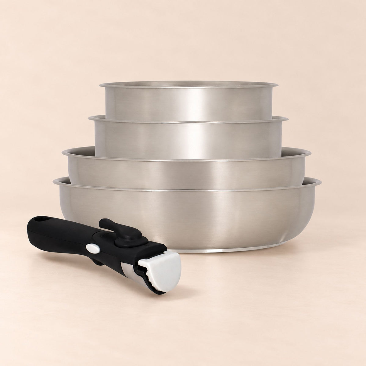 Set 4 casseroles iris inox empilées avec poignée amovible noire au premier plan sur fond beige