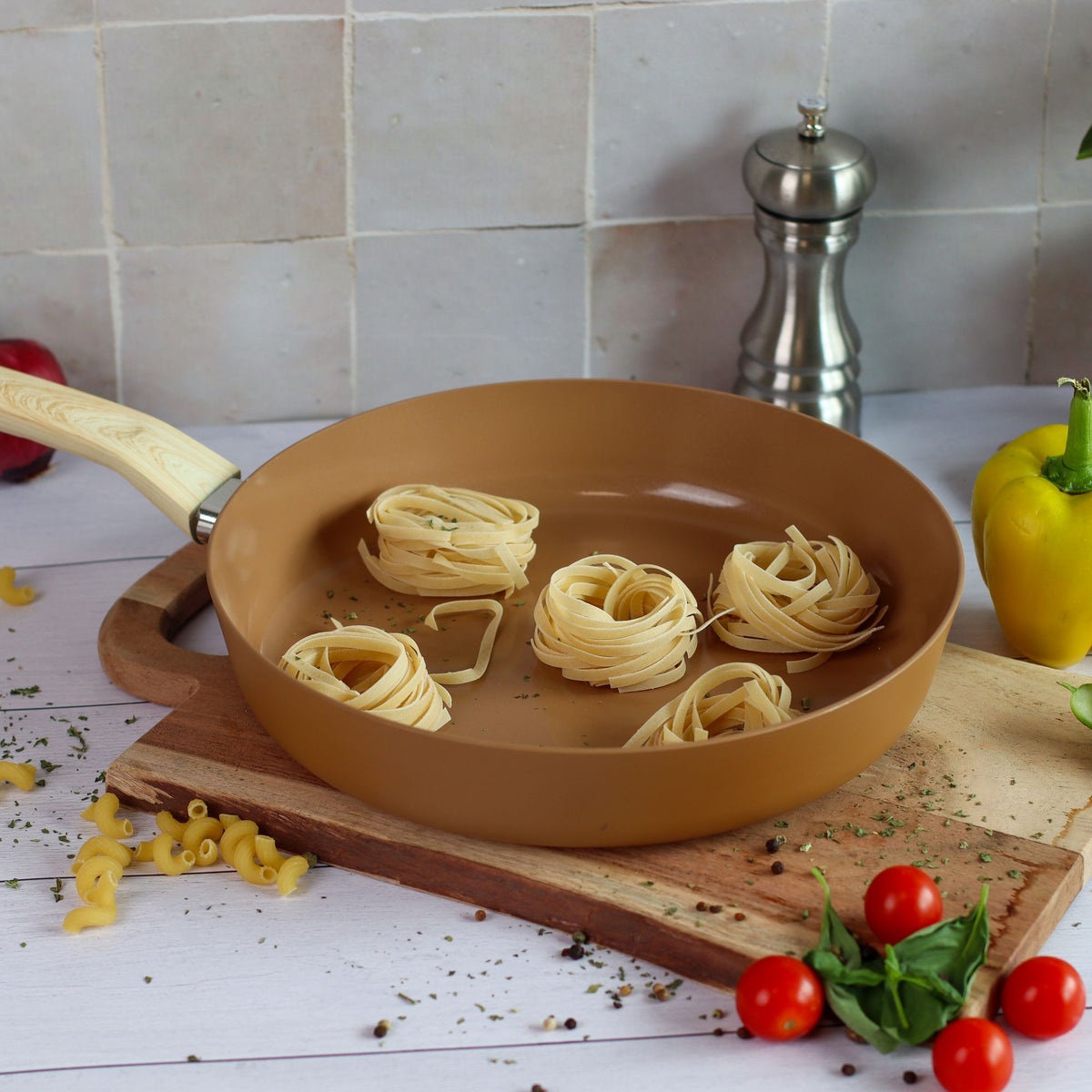 Poêle en aluminium colorée avec nests de tagliatelles, mise en scène cuisine sur planche en bois