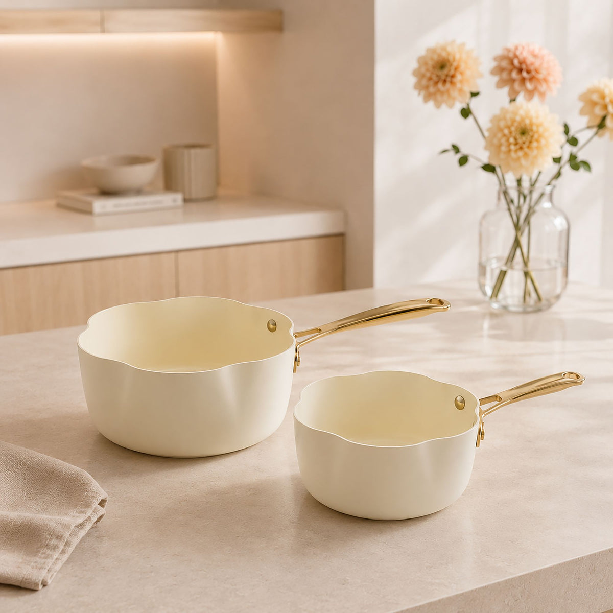 Casseroles Dahlia 20 cm beige crème avec poignées dorées, posées sur plan de travail marbre clair avec vase de fleurs