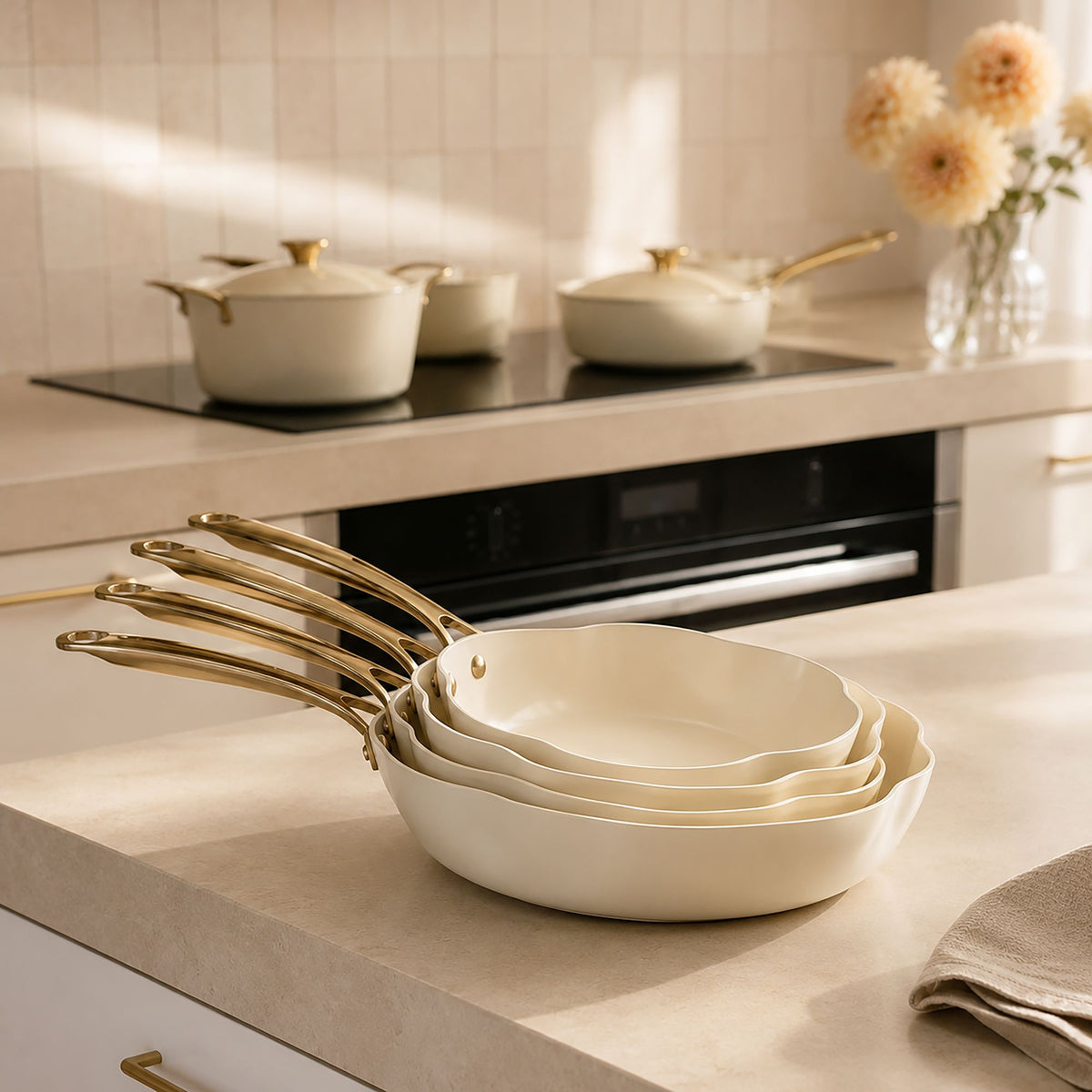 Set de 5 poêles Dahlia beige empilées, design floral, anses dorées, sur plan de travail cuisine moderne