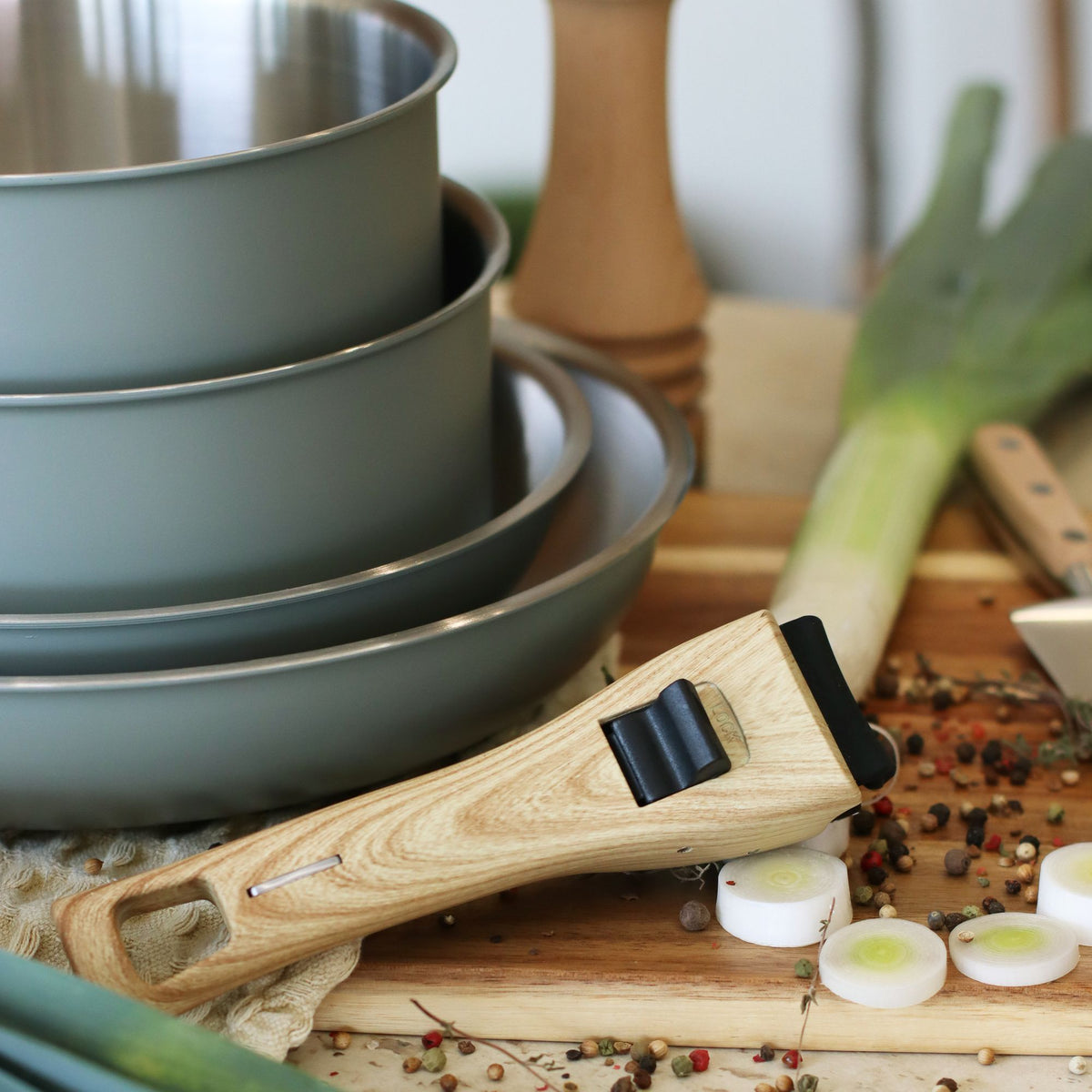 Set de 5 casseroles Easynox empilées bleu mat avec poignée amovible bois et ingrédients sur planche