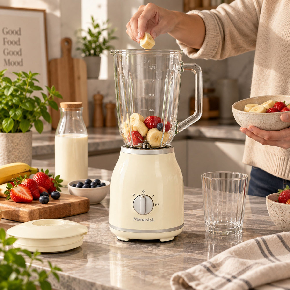 Blender rétro Menastyl 1,5L crème en préparation de smoothie fruits frais, main ajoutant banane dans le bol en verre