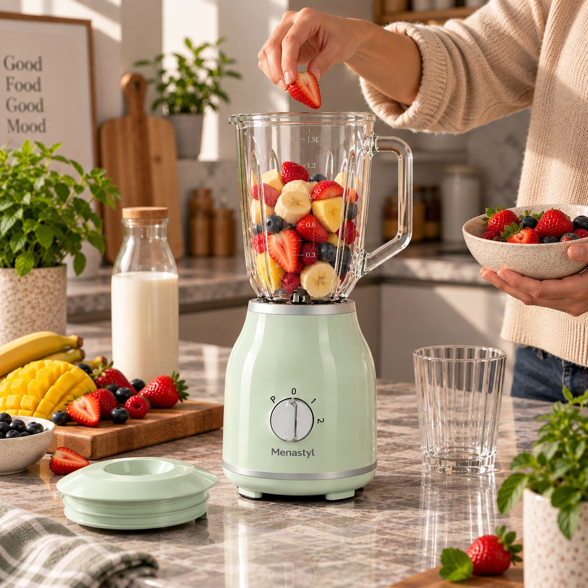 Blender rétro Menastyl 1,5L vert menthe avec fruits frais, main ajoutant une fraise dans le bol en verre