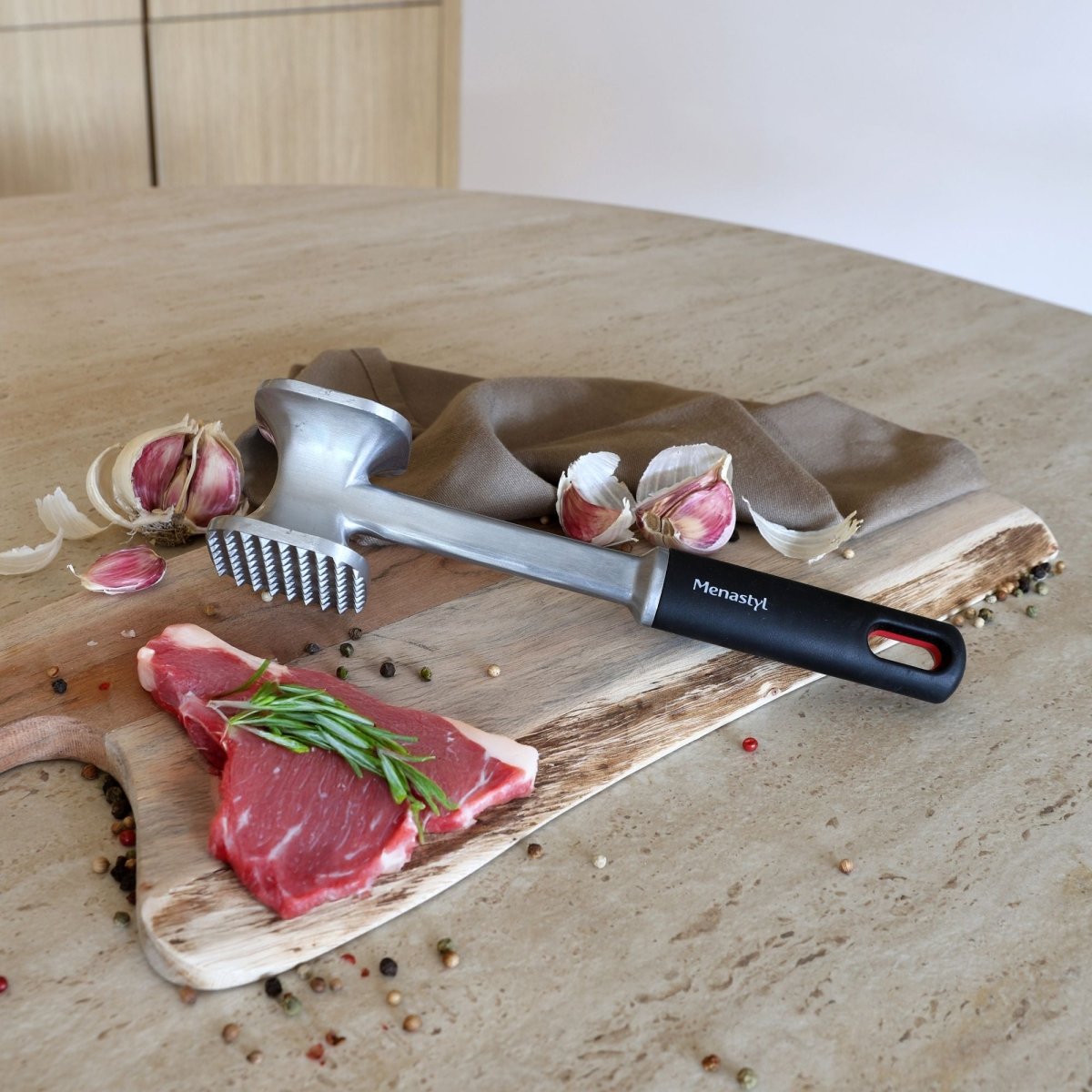 Attendrisseur de viande en aluminium avec manche noir et garniture d'ail sur planche de bois, vue d'ensemble de la mise en scène culinaire