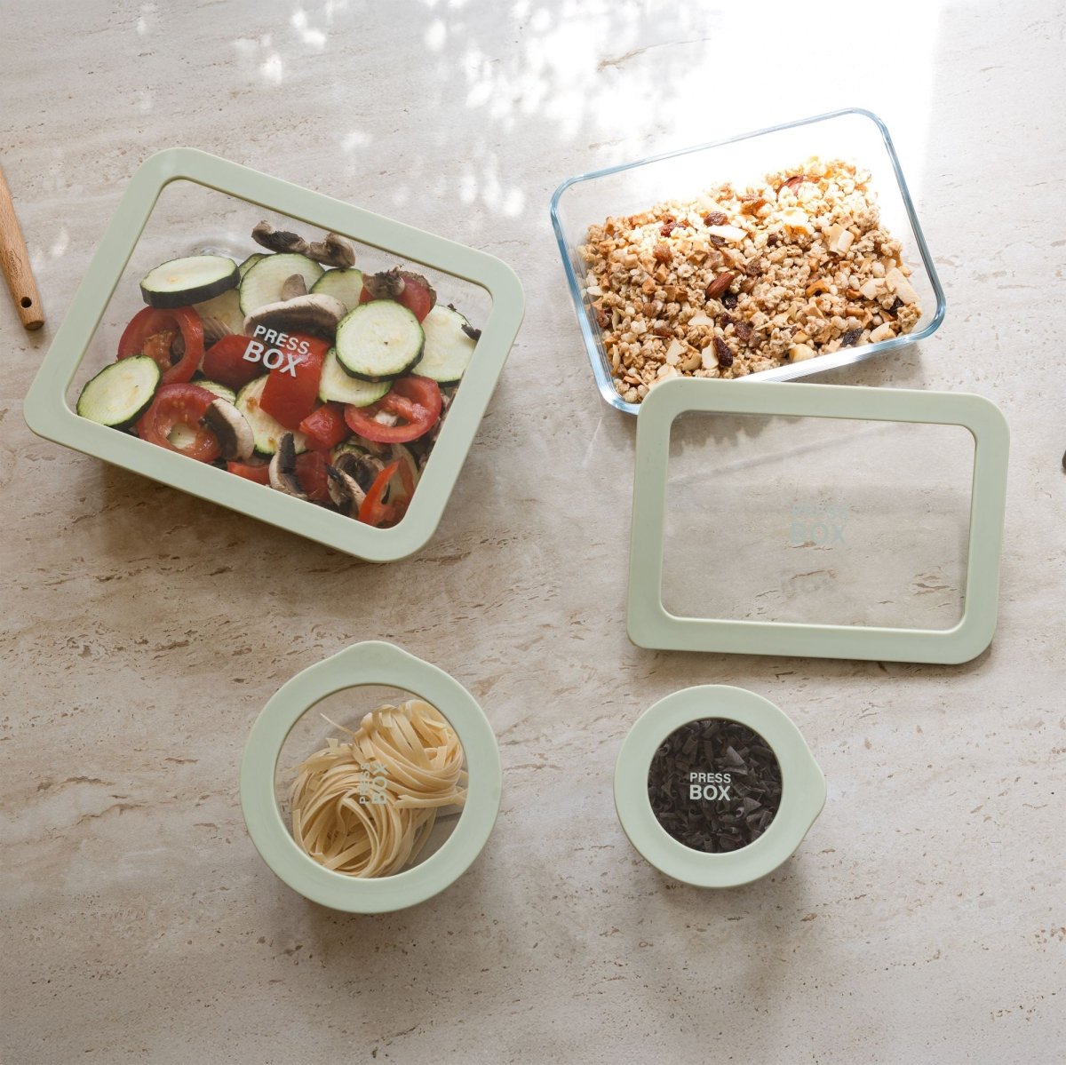 Vue d'ensemble des boîtes hermétiques rectangulaires Pressbox en verre avec couvercles verts contenant légumes, céréales et pâtes sur plan de travail