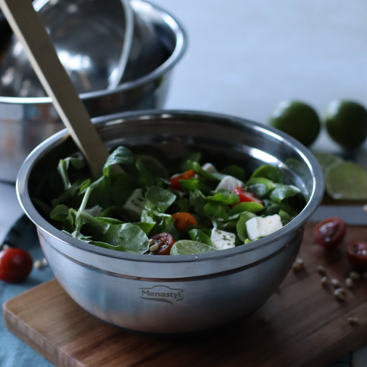 Bol à mélanger inox 18cm contenant une salade verte aux tomates cerises et feta, posé sur planche bois