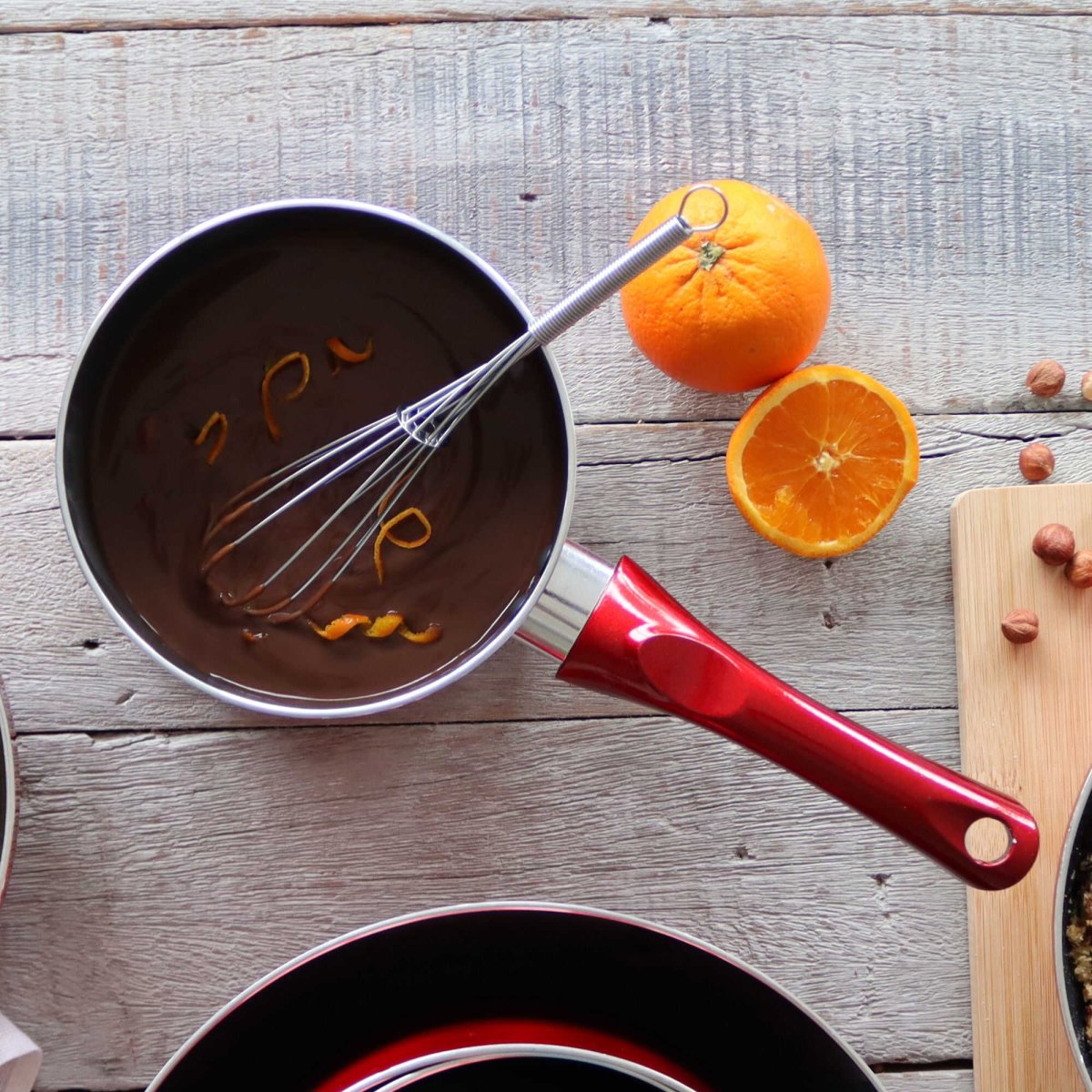 Casserole Cerise rouge 20cm en aluminium avec fouet, oranges et chocolat sur table en bois rustique