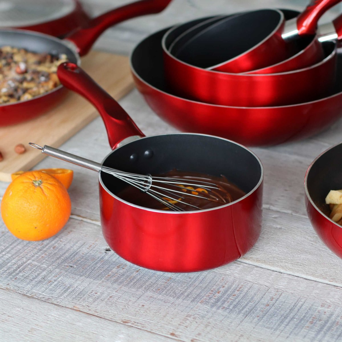 Set de casseroles Cerise rouges en aluminium avec revêtement antiadhésif noir, empilées sur plan de travail bois