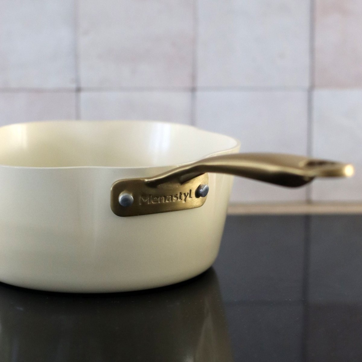 Vue détail du logo Menastyl gravé sur la poignée bronze de la casserole Dahlia 18 cm beige en aluminium recyclé