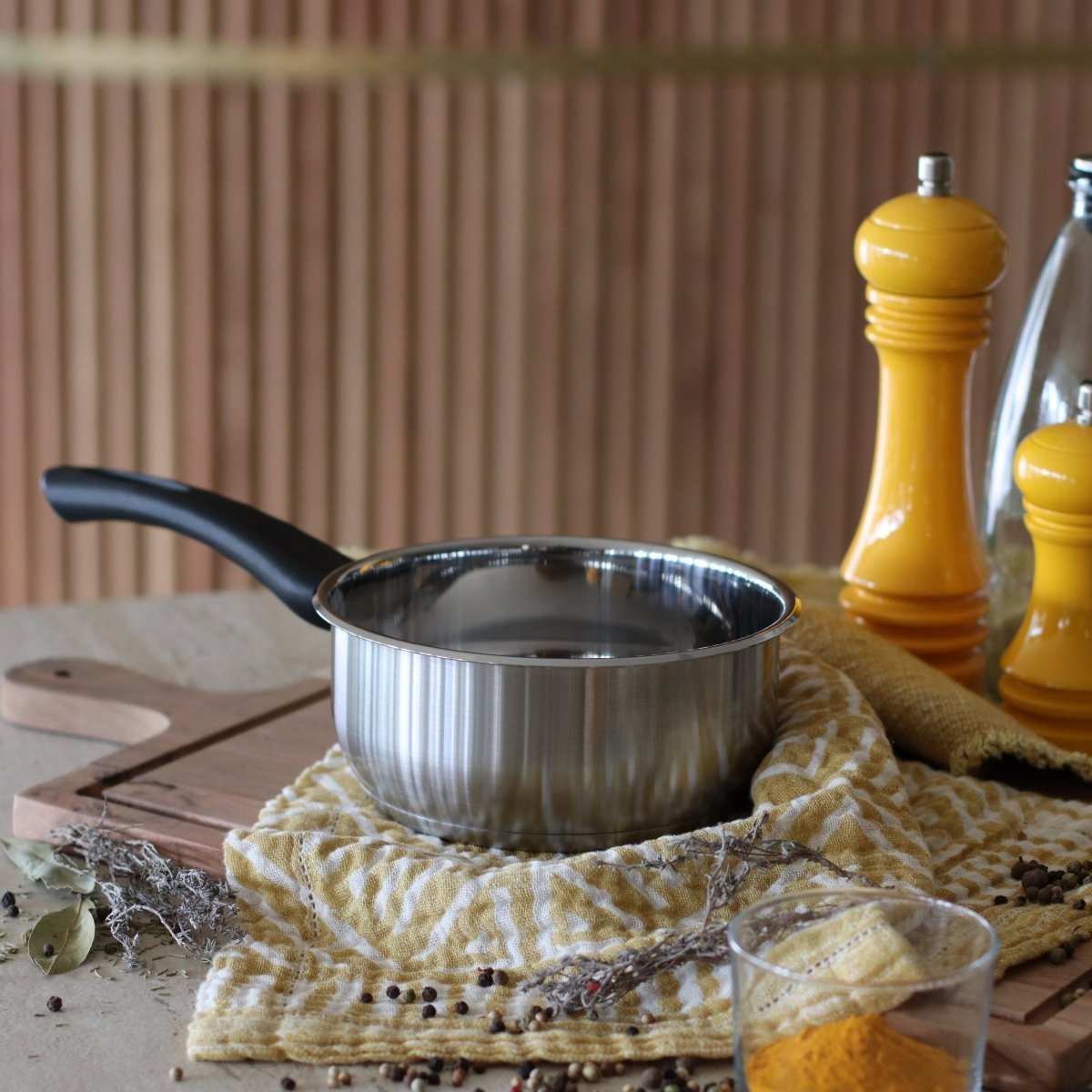 Casserole First 14 cm en acier inoxydable avec manche noir, posée sur torchon jaune avec assaisonnements