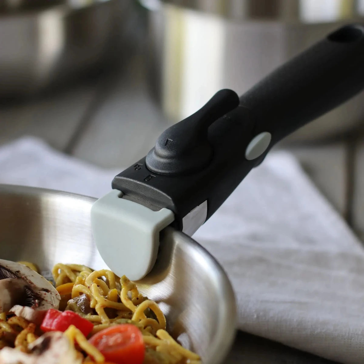Détail poignée amovible noire clipsée sur casserole inox Iris 16cm avec plat de pâtes