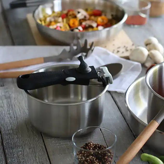 Casserole Iris 16cm en acier inoxydable avec poignée amovible noire, sur table en bois avec légumes en arrière-plan