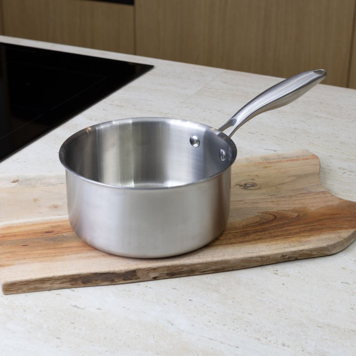 Casserole Trinox 18cm en acier inoxydable posée sur planche bois, vue de profil avec manche apparent