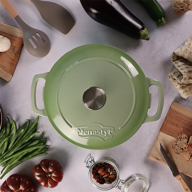 Vue de dessus cocotte ronde Colette 7L verte en fonte émaillée avec couvercle, entourée d'ingrédients et ustensiles de cuisine