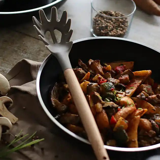 Cuillère à spaghettis en silicone blanc avec manche en bois dans une poêle de légumes colorés