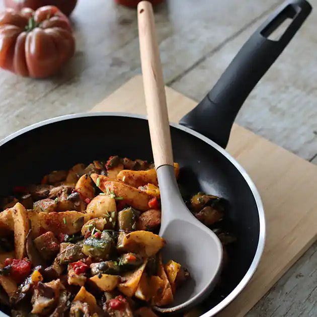 Cuillère Eliott en silicone blanc et manche bois dans poêle avec légumes sautés sur planche à découper