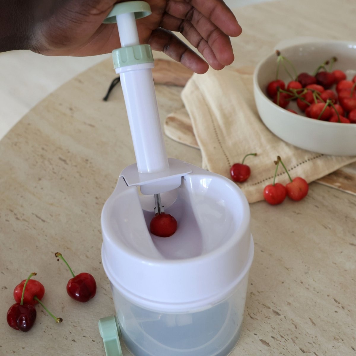 Utilisation du dénoyauteur à cerises en plastique blanc, main actionnant le mécanisme à ressort sur une cerise