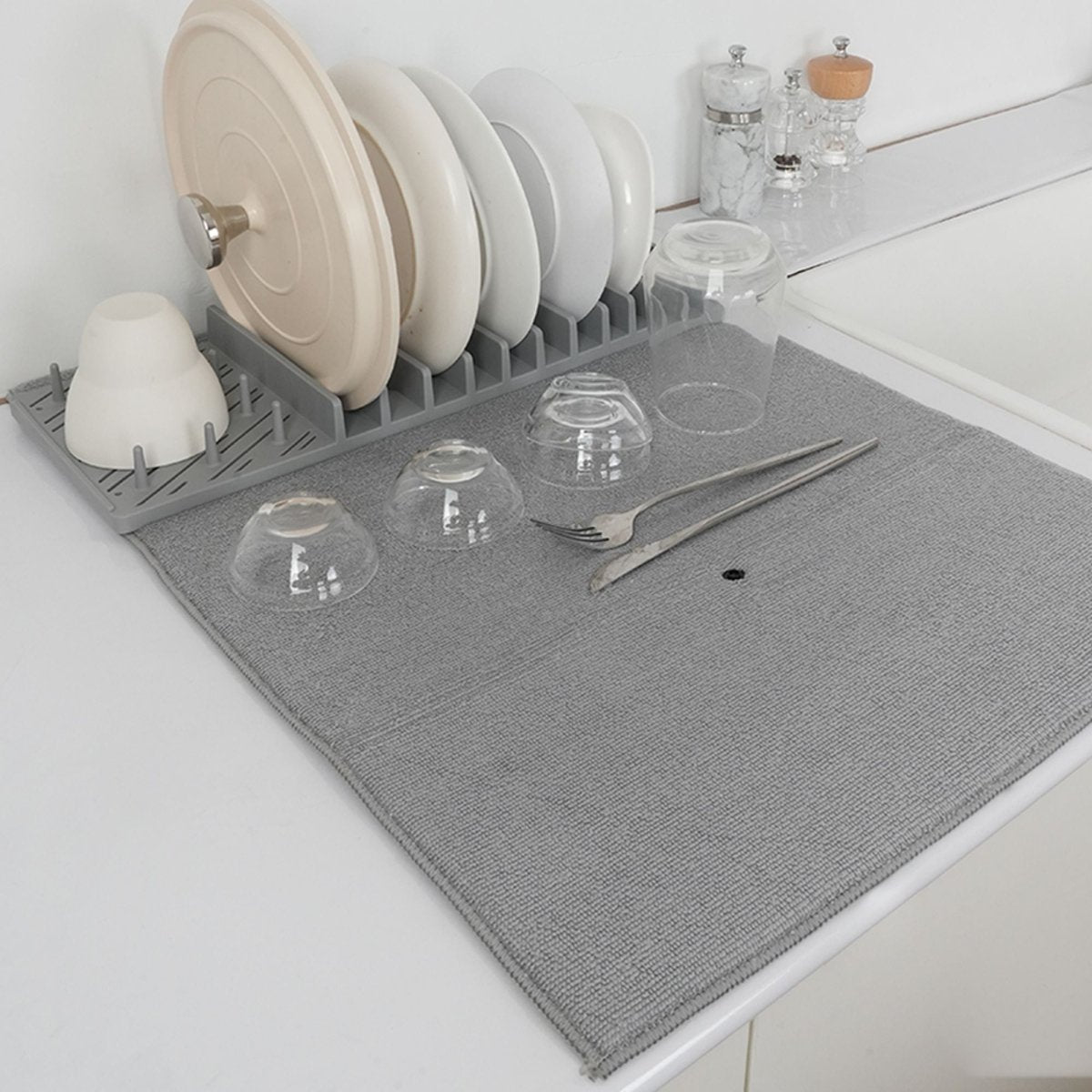 Égouttoir vaisselle gris avec tapis polyester, verres et couverts disposés sur plan de travail blanc