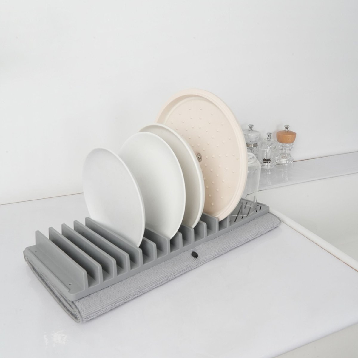 Égouttoir à vaisselle gris en polypropylène avec tapis absorbant, chargé d'assiettes et verres sur plan blanc