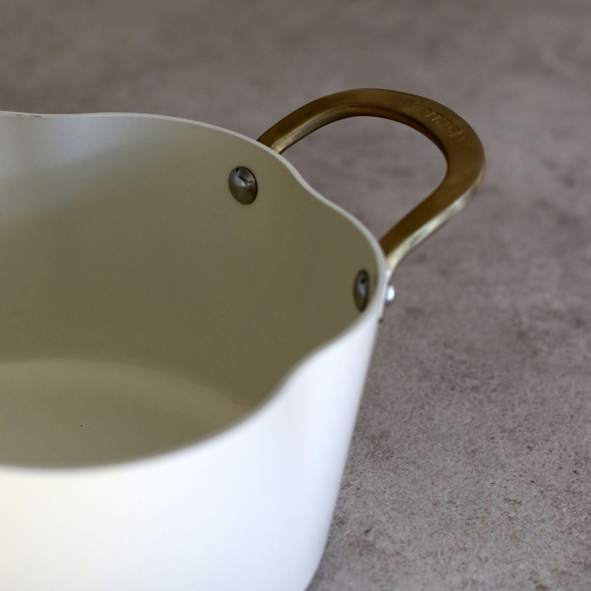 Gros plan sur la poignée bronze du faitout Dahlia 24 cm en aluminium recyclé beige avec rivets apparents