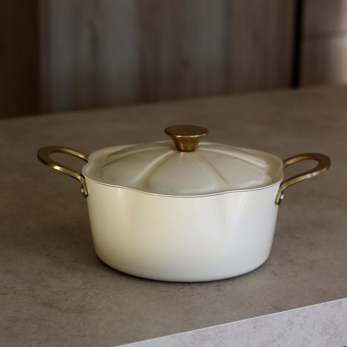 Faitout Dahlia 24cm beige avec couvercle et poignées dorées, posé sur plan de travail gris