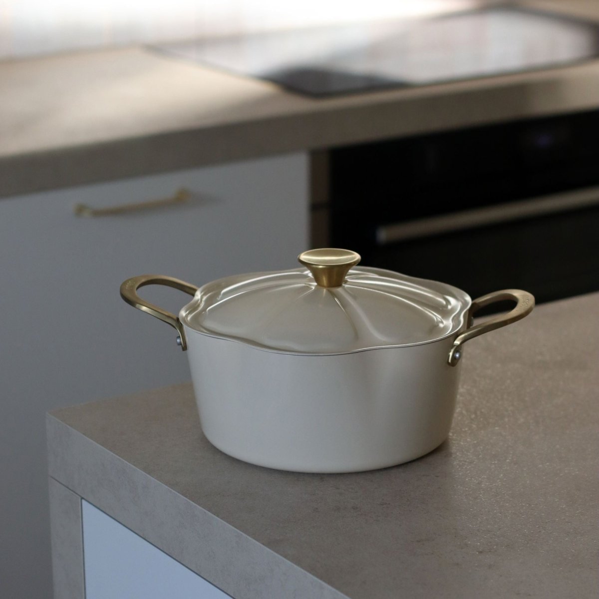 Faitout Dahlia 24cm beige en aluminium recyclé avec couvercle et poignées dorées sur plan de travail