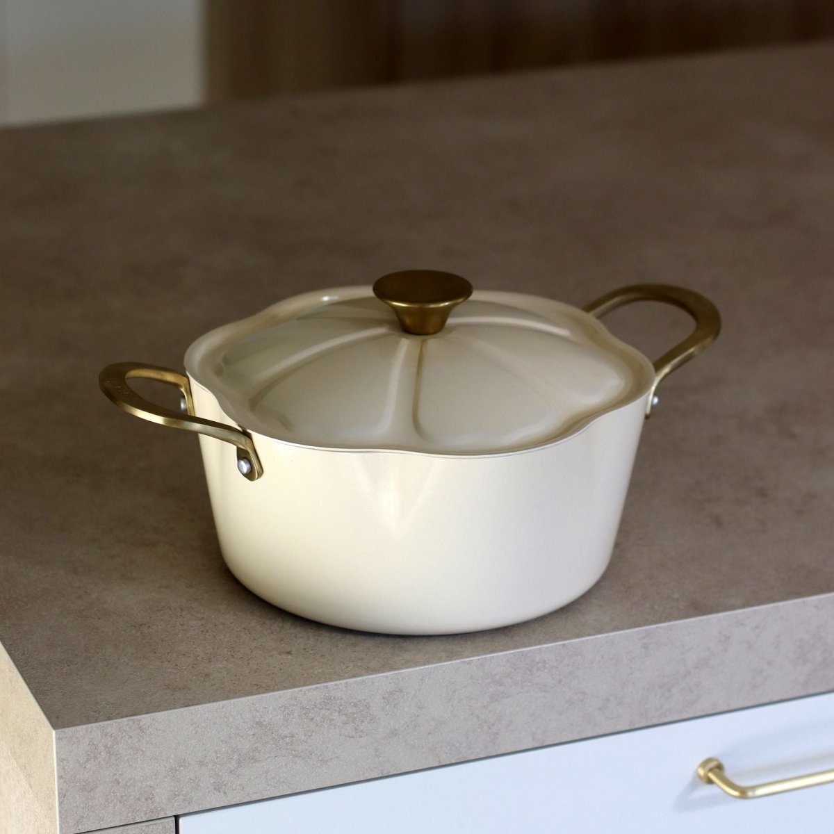 Faitout Dahlia 24 cm beige avec couvercle et poignées dorées, posé sur plan de travail gris clair