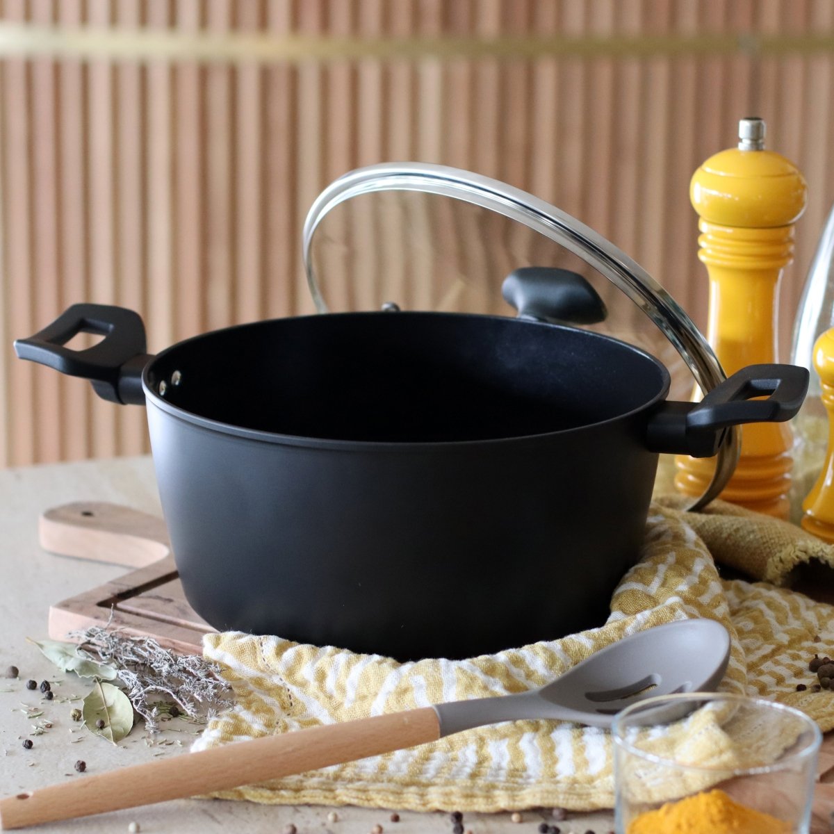 Faitout First 24cm noir avec couvercle en verre, ambiance culinaire avec accessoires de cuisine sur fond bois
