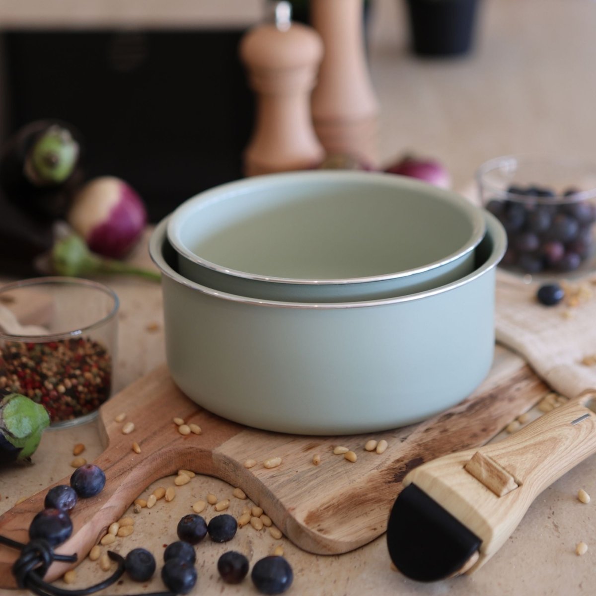 Lot de 2 casseroles Colorama 16 et 18 cm empilées, finition vert sauge, sur planche en bois avec ingrédients