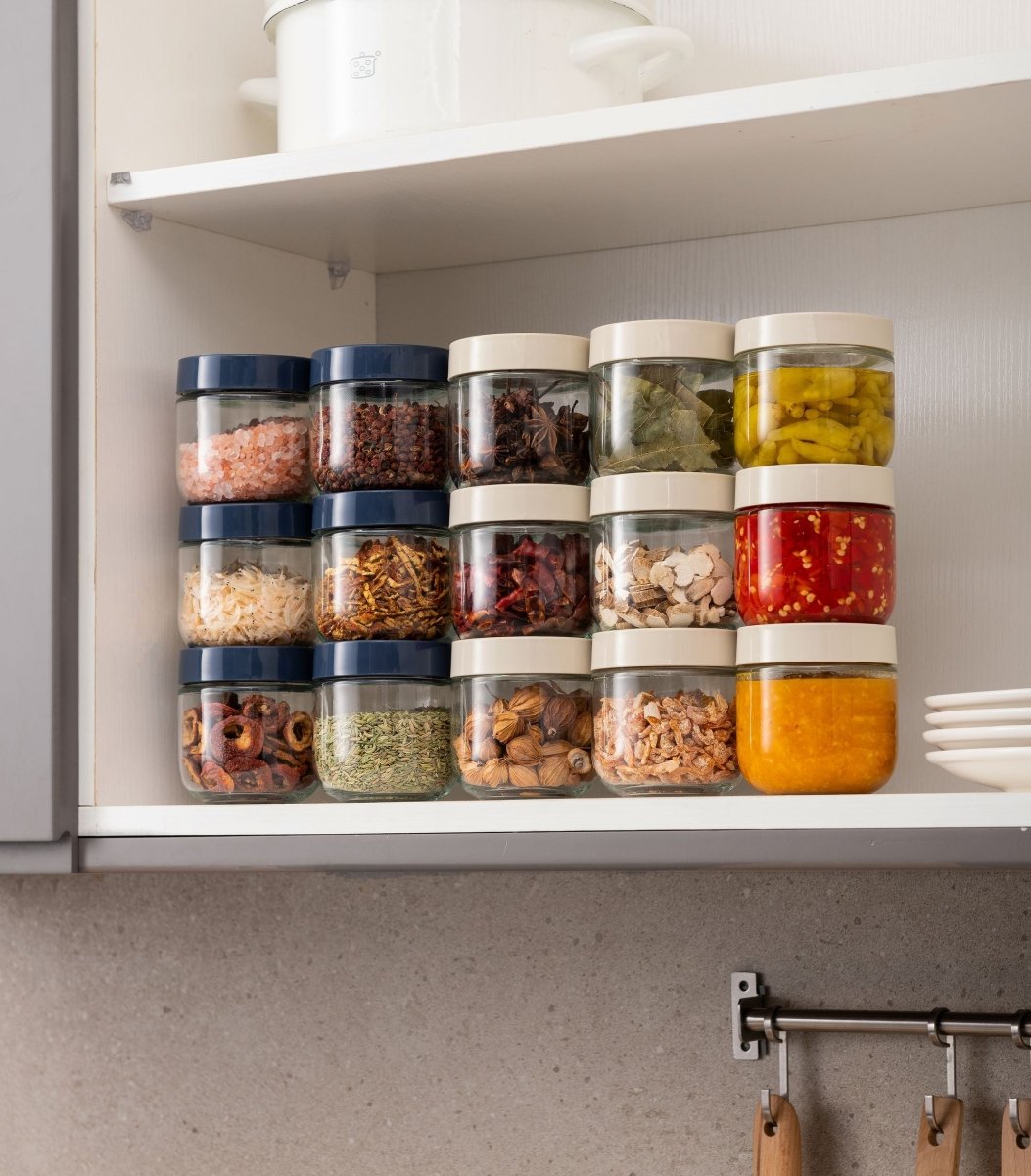 Boîtes hermétiques en verre empilées dans placard de cuisine, couvercles colorés bleu et blanc, organisation optimale des épices et condiments