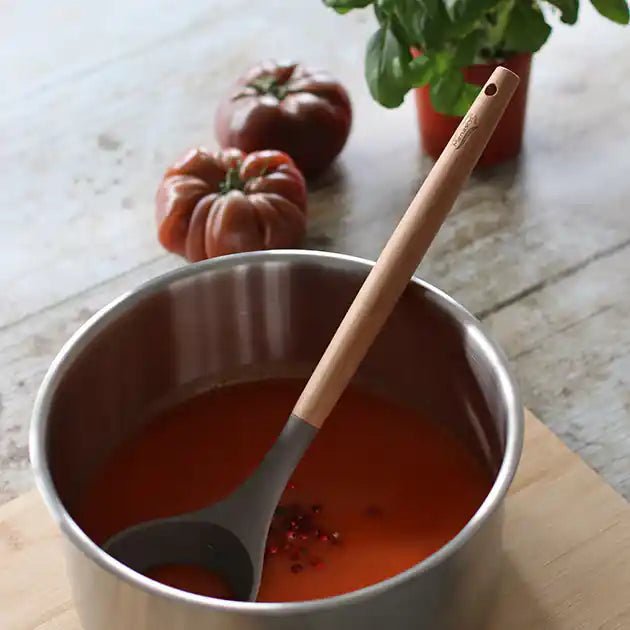Louche Eliott en silicone gris et bois dans casserole de sauce tomate, avec tomates fraîches en arrière-plan