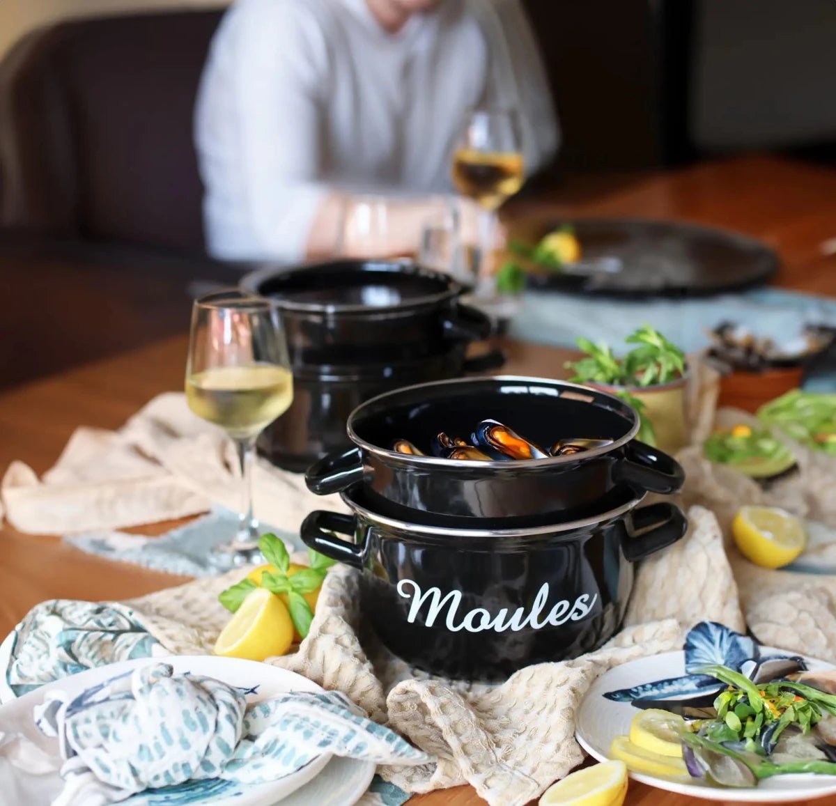 Marmite à moules noire en acier émaillé 24cm avec moules cuites, accompagnée de vin blanc et citron sur table