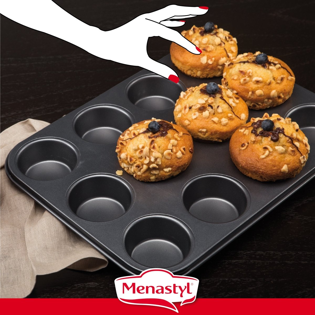 Moule à 12 muffins Amandine en acier carbone avec muffins aux noix et myrtilles, main illustrée les retirant