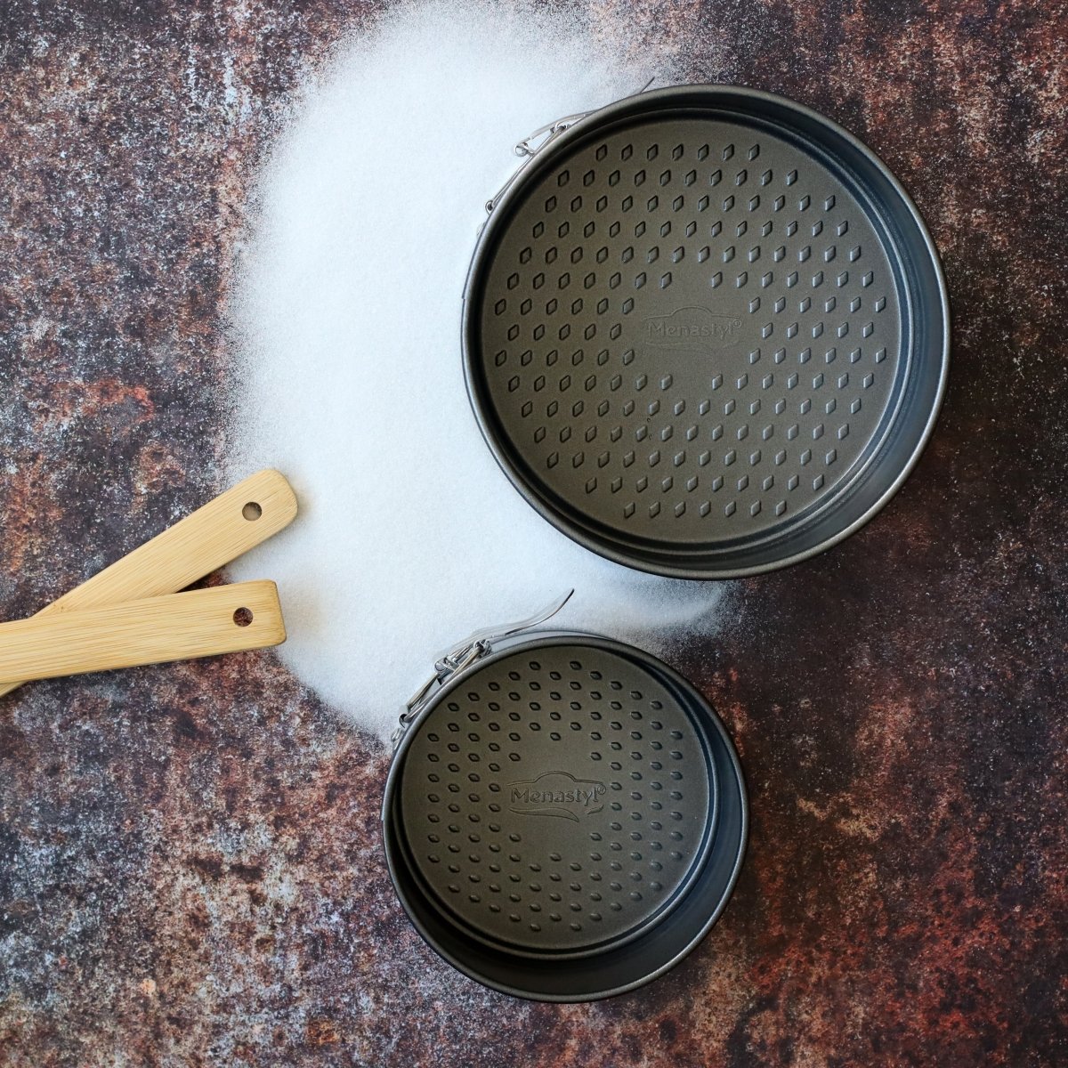Deux moules à charnière Amandine en acier noir et spatules en bois, vue du dessus sur fond clair