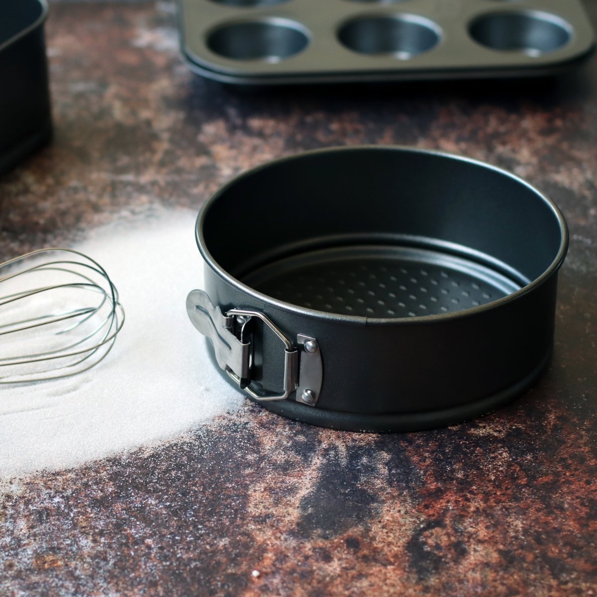 Moule à charnière Amandine 24 cm en acier noir avec clip métallique, posé sur plan de travail avec fouet