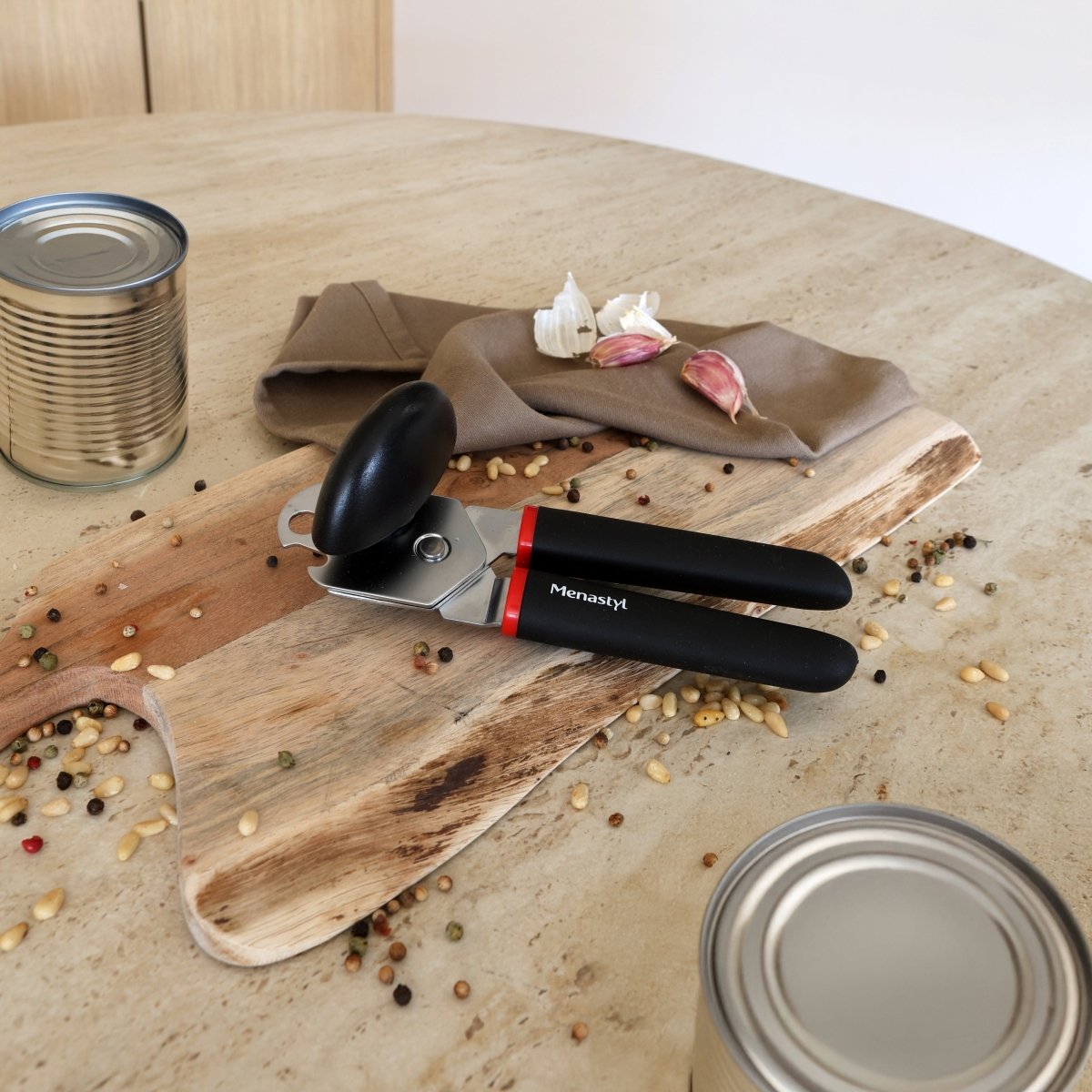 Ouvre-boîte multifonction en acier inoxydable avec manches noires, posé sur planche bois avec conserves et ingrédients