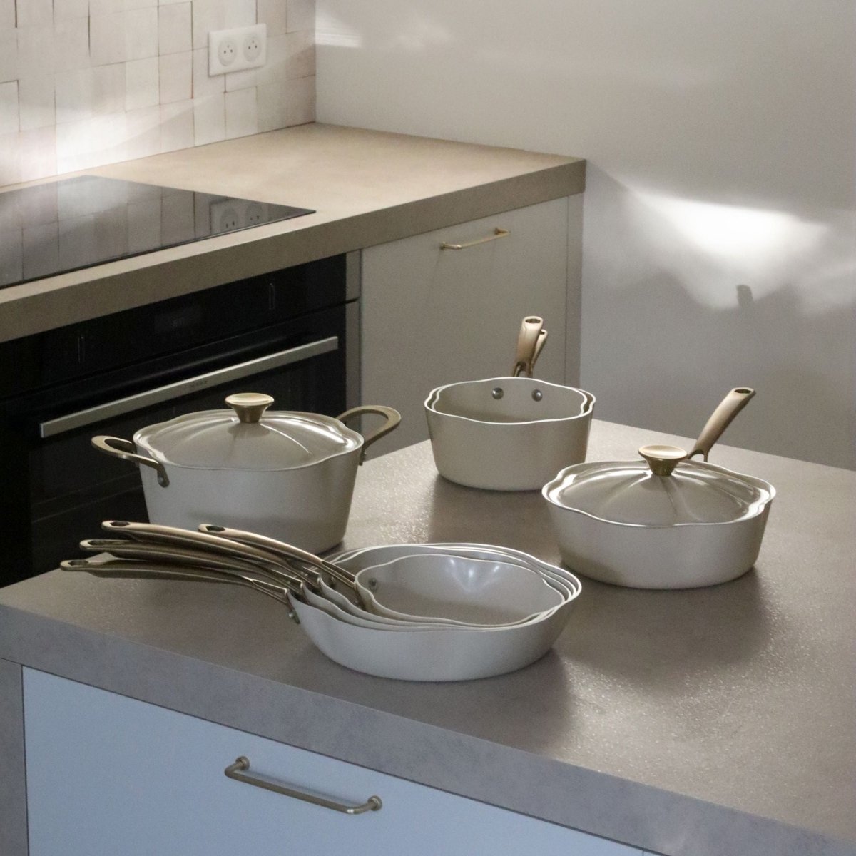 Collection complète poêles et casseroles Dahlia beige en aluminium recyclé, disposée sur plan de travail cuisine moderne