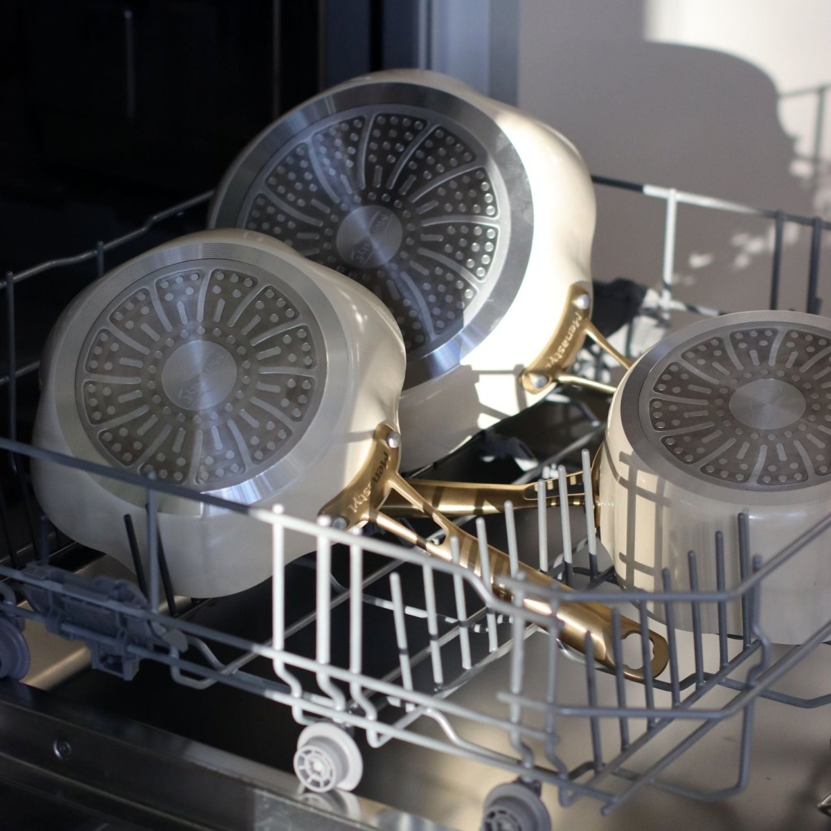 Trois poêles Dahlia beige en aluminium recyclé placées dans un lave-vaisselle, vue intérieur avec motif dahlia