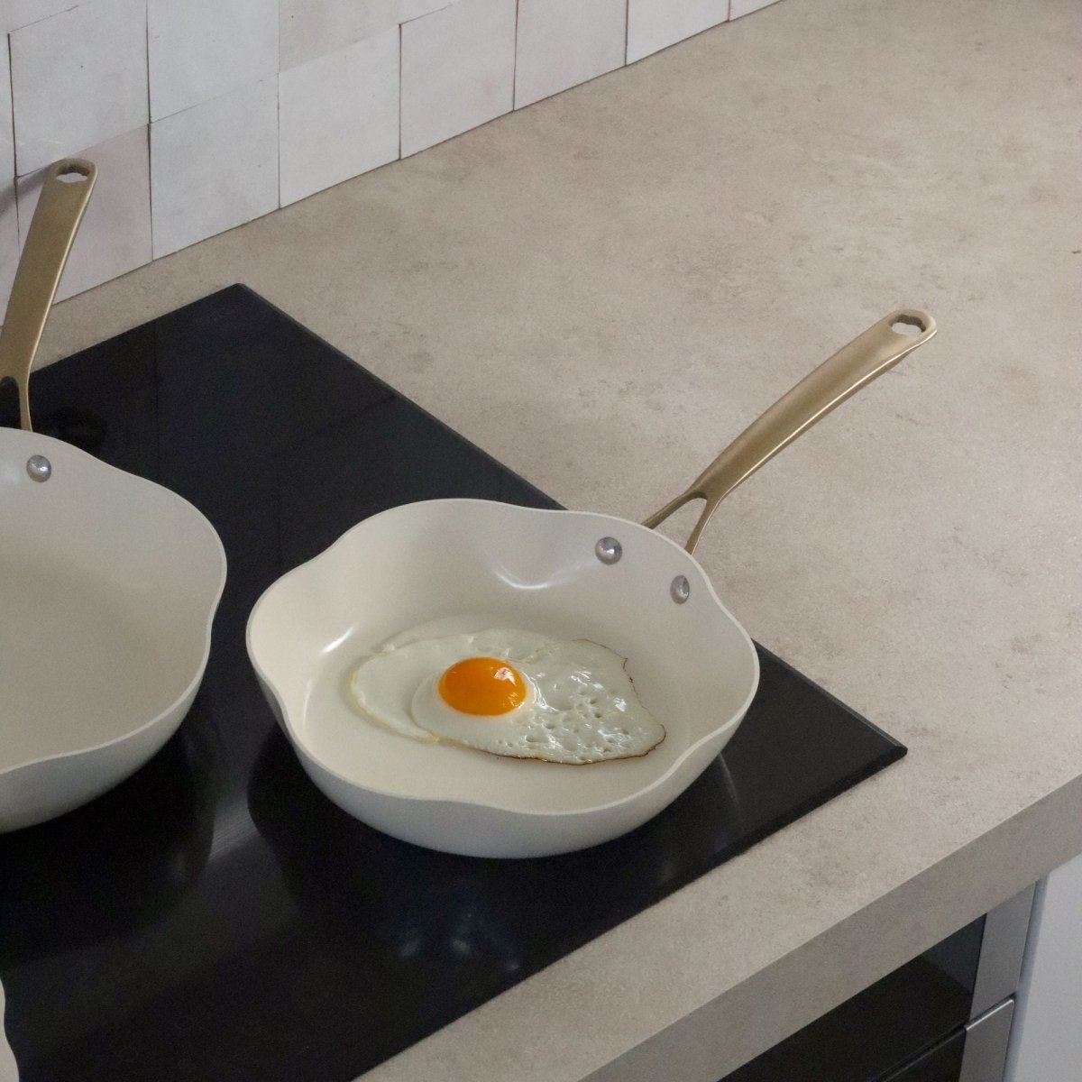 Poêle Dahlia 20 cm beige avec œuf au plat en train de cuire, posée sur plaque à induction noire