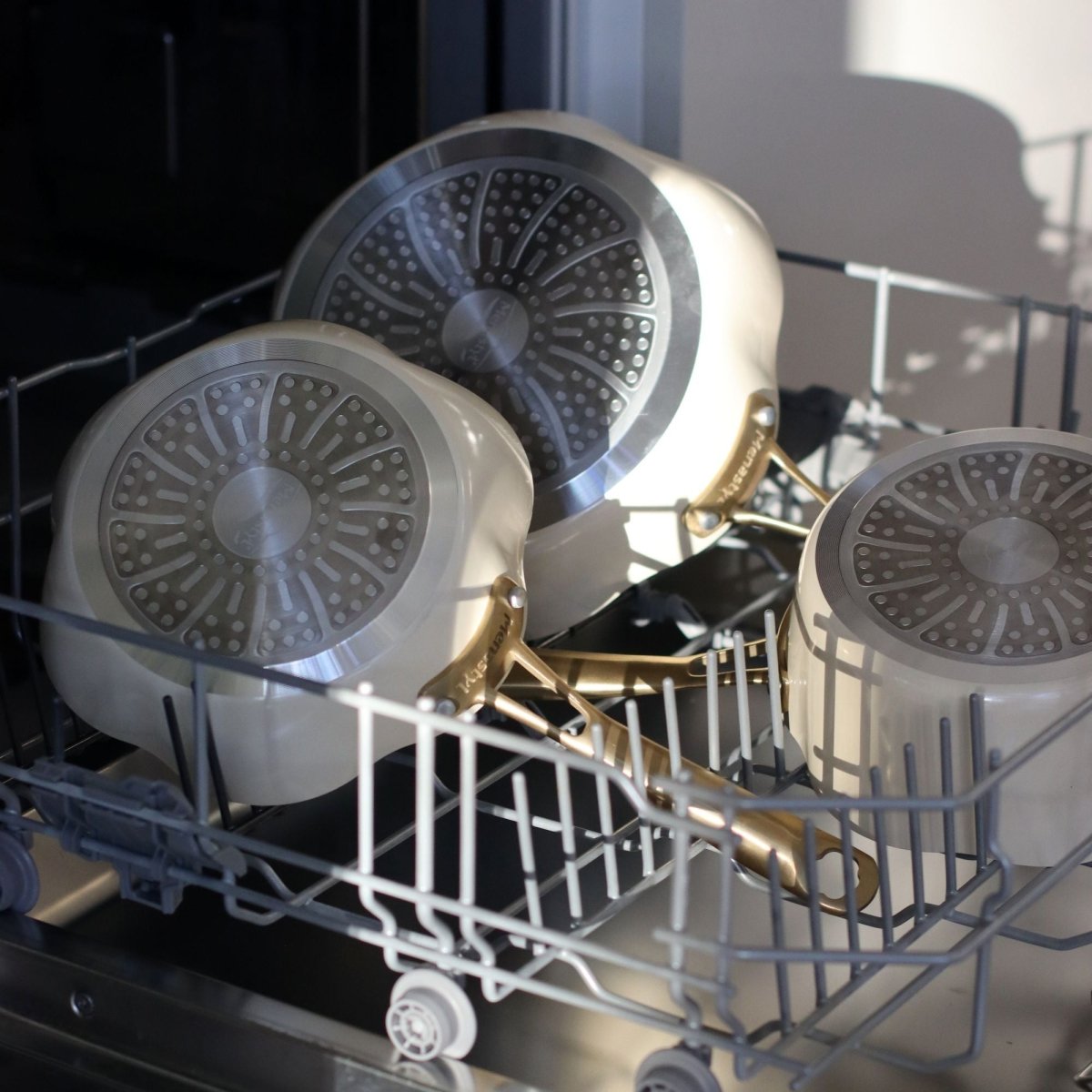 Trois poêles Dahlia beige en aluminium recyclé dans un lave-vaisselle, montrant le motif intérieur en forme de fleur