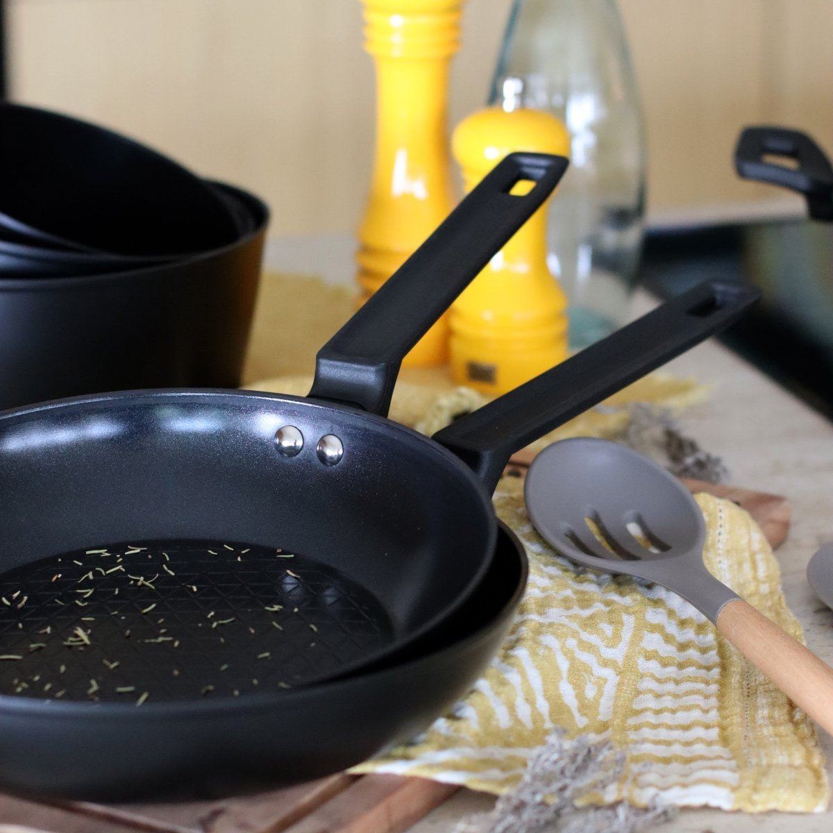 Poêle First 30 cm en aluminium noir avec ustensiles de cuisine sur torchon jaune à motifs