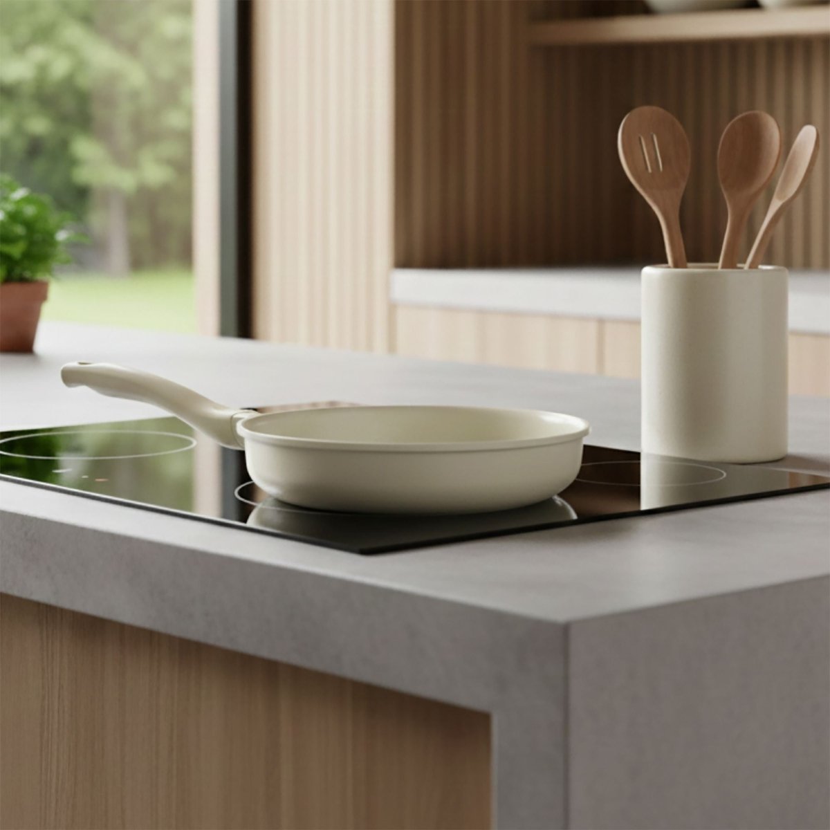 Poêle Pure 24cm crème en fonte d'aluminium recyclé posée sur plaque induction avec ustensiles en arrière-plan