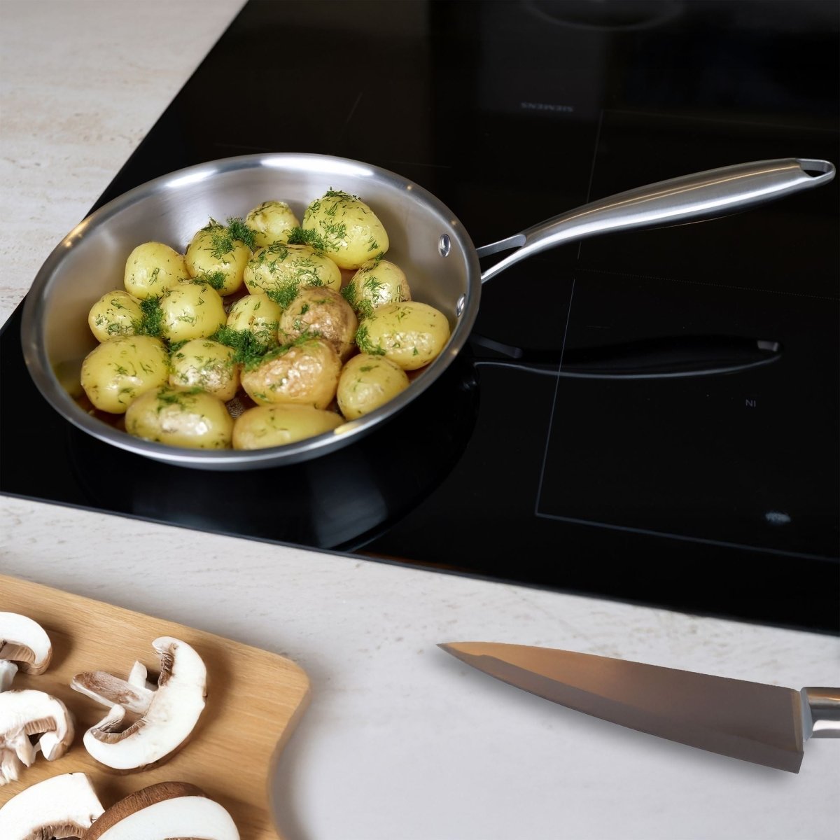 Poêle Trinox 24cm en inox avec pommes de terre persillées sur plaque induction noire