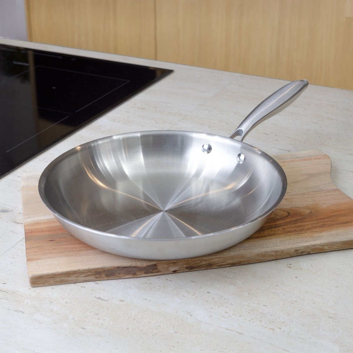 Poêle Trinox 28cm en acier inoxydable posée sur planche bois, vue intérieur avec rivets apparents