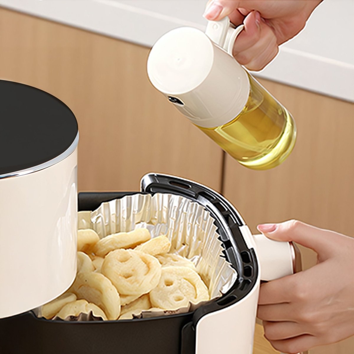 Pulvérisateur d'huile en verre versant de l'huile sur des aliments dans une friteuse à air chaud