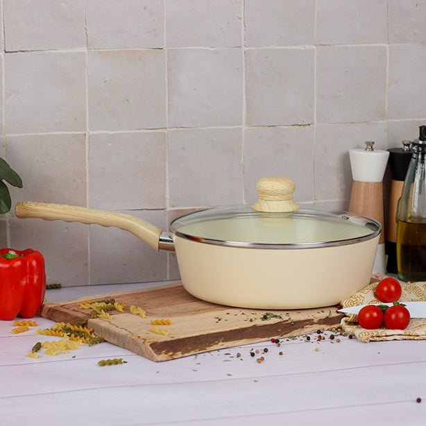 Sauteuse Colorama 24cm beige avec couvercle en verre, mise en scène sur plan de travail avec légumes et pâtes