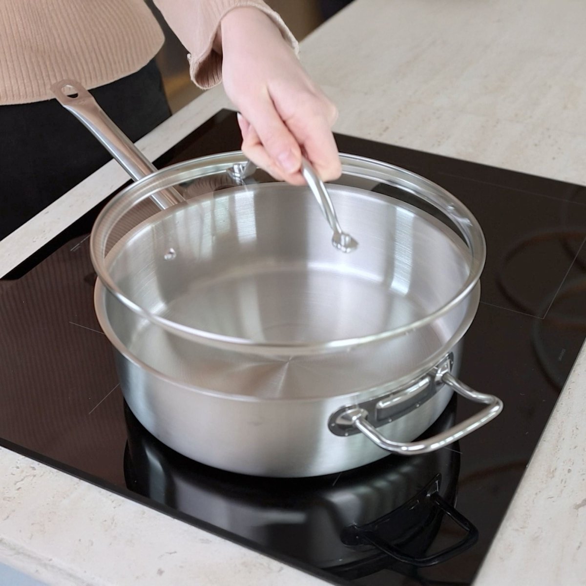 Sauteuse professionnelle 28cm en acier inoxydable avec couvercle en verre, vue de dessus sur plaque de cuisson