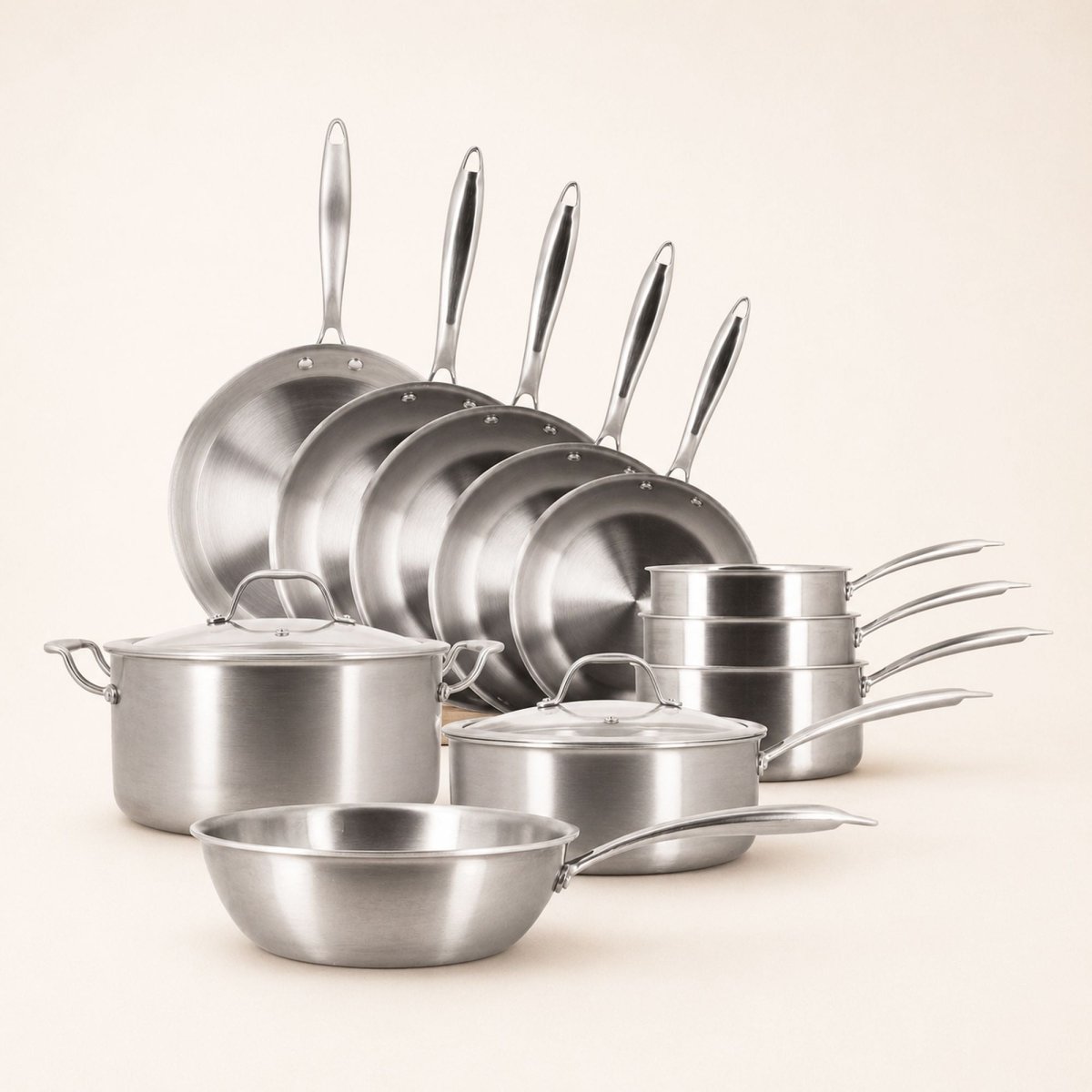 Set complet 11 pièces Triply Menastyl en acier inoxydable : poêles, casseroles, wok et faitout disposés sur fond beige