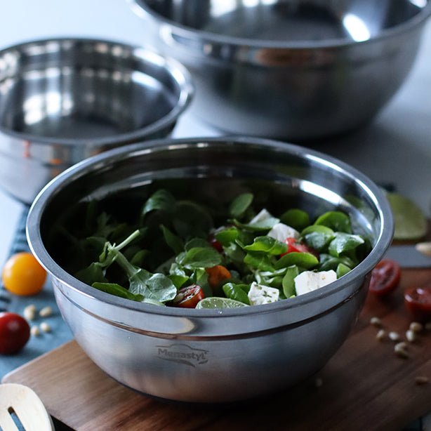 Bol à mélanger en acier inoxydable avec salade verte, posé sur planche en bois, vue rapprochée